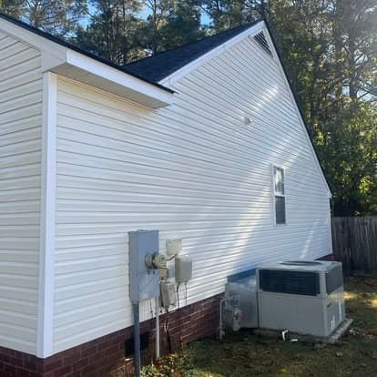 White vinyl siding home with air conditioning unit and utility meter featured in a green backyard.