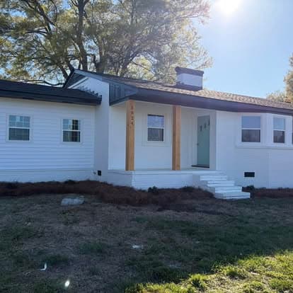 Modern white house with wooden accents and front steps, surrounded by greenery.