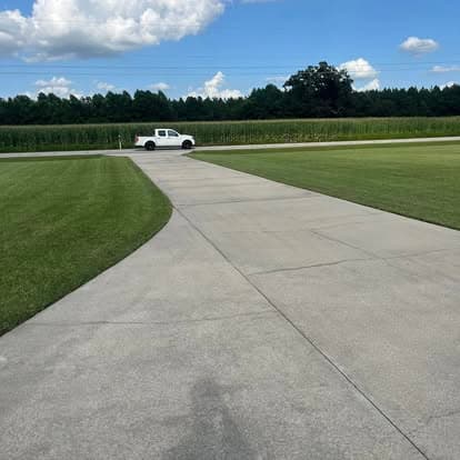 White pickup truck on a curved concrete driveway with green grass and cornfield in background.