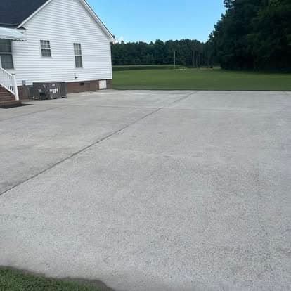 Spacious concrete driveway beside a large white house in a green outdoor setting.
