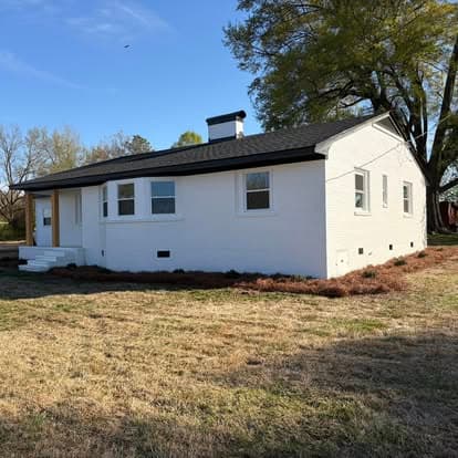 Modern white house with a black roof surrounded by grass and trees on a sunny day.