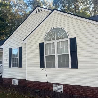 White house exterior featuring arched window and black shutters against a wooded backdrop.