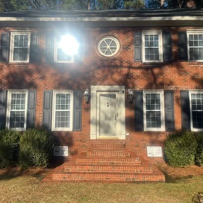 Two-story brick home with a circular window, white door, and lush green shrubs.