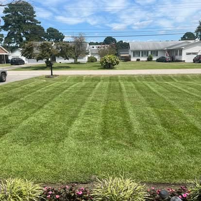 Lush green lawn with freshly mowed stripes and landscaped flower beds under a blue sky.