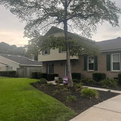Two-story brick house with green shutters, landscaped yard, and for sale sign in front.