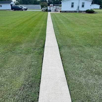 Concrete walkway leading through a well-maintained grassy lawn towards a white house.